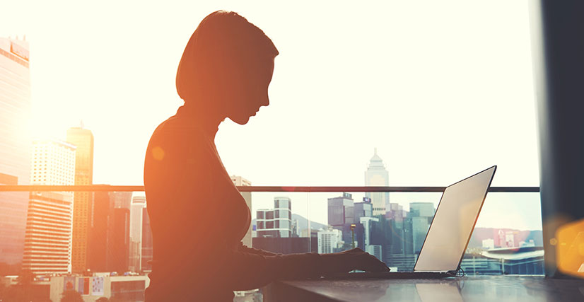 Woman sitting at table on laptop with city skyline in background